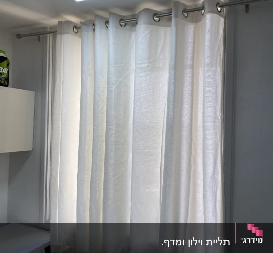 וילון לבן תלוי על מוט מתכת בחדר מואר